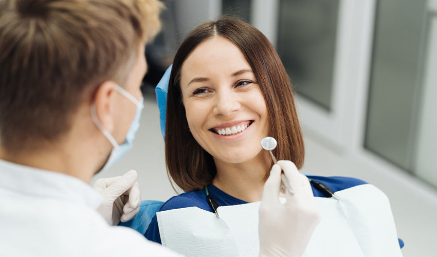 Smiling patient sitting in a dental chair while a dentist holds a dental mirror